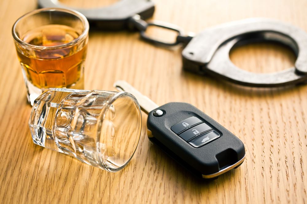 Car keys next to empty shot glass, with handcuffs in background